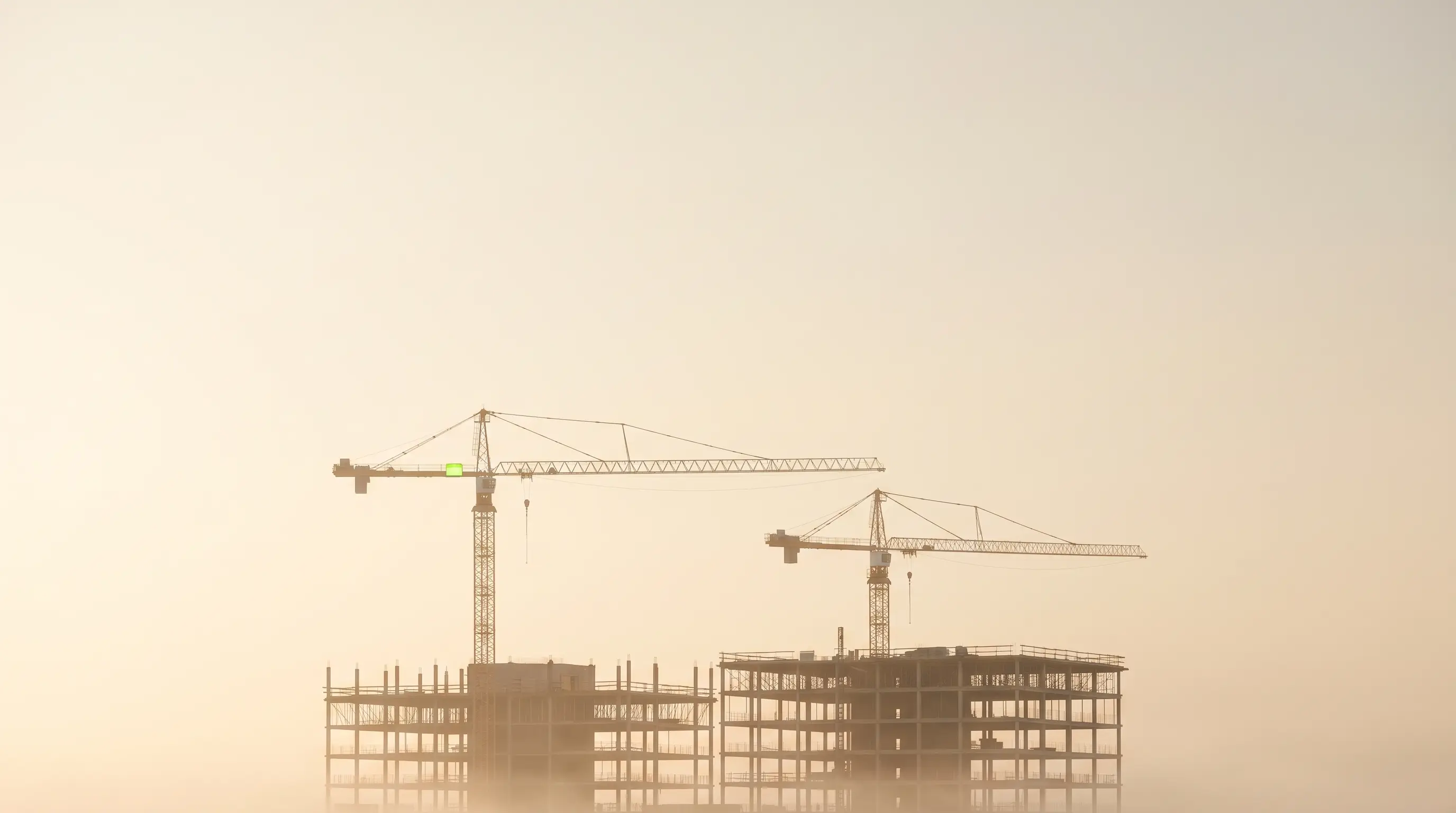 Tower cranes over a site at dawn, in warm haze